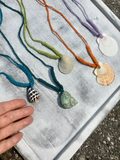 Colorful necklaces with shell pendants on a textured surface. my hand is on the picture to illustrate the size of the shell pendants.