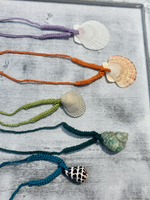 Five crocheted necklaces with shells on a textured surface