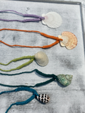Five crocheted necklaces with shells on a textured surface