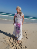 Woman in a floral dress standing on a sandy beach with ocean waves in the background