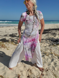 Woman in a tie-dye dress standing on a sandy beach with ocean in the background