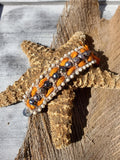 Bracelet with orange, black, and white beads on a wooden surface