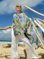Person wearing a colorful dress and sunglasses on a beach with driftwood.