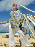 Person wearing a colorful dress and sunglasses on a beach with driftwood.