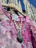 a pink ice dye top with a necklace featuring a large grey oyster shell pendant and white pearl beads, against a wooden fence background.