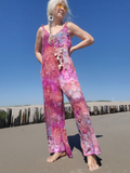 Person wearing a colorful tie-dye jumpsuit standing on a beach with a clear blue sky.