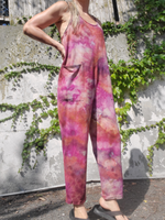 Person wearing a colorful tie-dye jumpsuit standing against a wall with greenery.