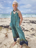 Woman in a teal linen jumpsuit standing on a beach with ocean in the background