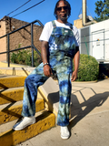 Person wearing tie-dye overalls sitting on steps outdoors
