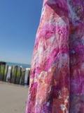 Close-up of a colorful floral dress with a beach and wooden pier in the background.
