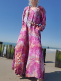 Person wearing a long, colorful dress on a beach with clear blue sky.