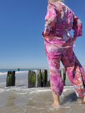 Person wearing a pink tie-dye outfit standing on a beach with a clear blue sky.