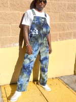 Person wearing blue tie-dye overalls standing against a beige wall.