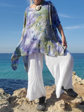 Person wearing a colorful top and white pants standing on rocks by the ocean.