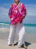 I'm wearing a pair of white linen pants with this bright pinkish ice dye kaftan, hands in my pockets