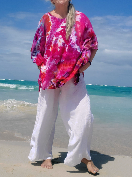 I'm wearing a pair of white linen pants with this bright pinkish ice dye kaftan, hands in my pockets