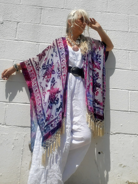 Woman wearing a kimono with floral patterns and fringe against a white wall.