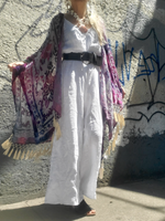 Person wearing a white outfit with a colorful kimono against a graffiti-covered wall.