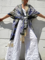 Person wearing a floral kimono-style garment with tassels against a white wall.