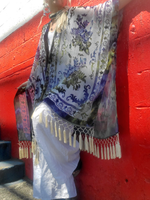 Person wearing a patterned kimono with fringes, and white pants against a red wall.