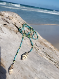 Necklace with shell pendants on a piece of driftwood by the ocean