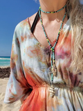 Person wearing a colorful dress and beaded necklace on a beach