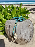 Beaded necklace on a piece of driftwood with a beach and ocean background