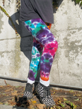 Person wearing colorful tie-dye leggings standing against a concrete wall.