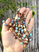 Hand holding a necklace with multicolored beads against a wooden fence background