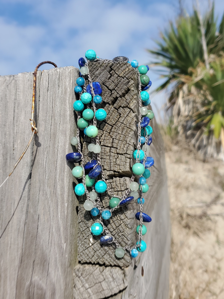 Beaded necklace with blue and green beads on a wooden post with a natural background
