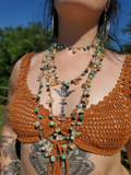 A close-up of a person outdoors wearing a rust-orange crochet halter-style top and layered beaded necklaces with turquoise, green, brown, and amber beads.