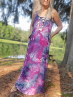 Woman wearing a colorful tie-dye dress standing outdoors near trees and a pond.