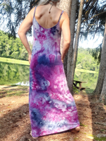 woman wearing a tie-dye dress in a natural setting with trees and a lake. a back shot