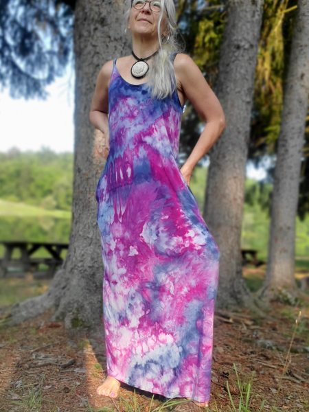 Woman wearing a tie-dye dress standing in a forested area with trees and grass in the background.