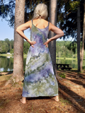 Woman wearing an ice-dye dress standing in a forest with a lake in the background. a back shot