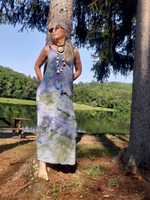 Woman in a tie-dye dress standing by a lake with trees in the background