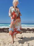 Woman in a colorful dress standing on a beach with blue sky and ocean.