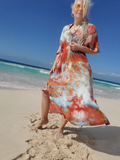 Woman in a colorful dress standing on a beach with clear blue sky and ocean.