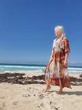 Woman in a tie-dye dress standing on a beach with clear blue sky and ocean.