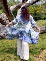 Person wearing a tie-dye dress standing in a natural setting with trees and grass.