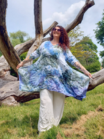 Woman in a tie-dye dress standing next to a large tree branch in a natural setting