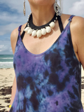 Person wearing a purple tie-dye tank top with a necklace on a beach.