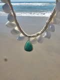 Necklace with a green pendant on a white shell against a beach background