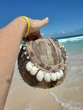 Hand holding a coconut shell with necklace against a beach background