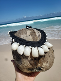 Coconut shell with a black and white beaded necklace held on a beach
