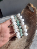 Hand holding a beaded shell bracelet with white and amazonite beads on a textured surface.