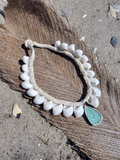 Necklace with white beads and a green pendant on a textured surface