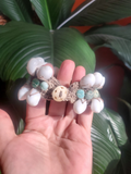 Hand holding a beaded bracelet with aqua and white beads against a leafy background