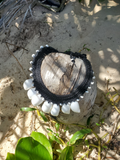 Black cord crocheted shell necklace on a coconut with sand and grass in the background