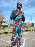 Person wearing colorful tie-dye overalls and sunglasses outdoors.